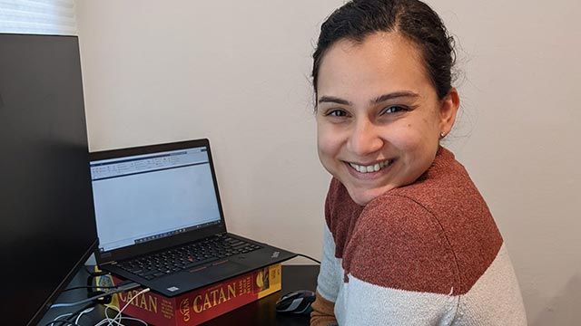 Woman smiling with laptop on the desk behind her.
