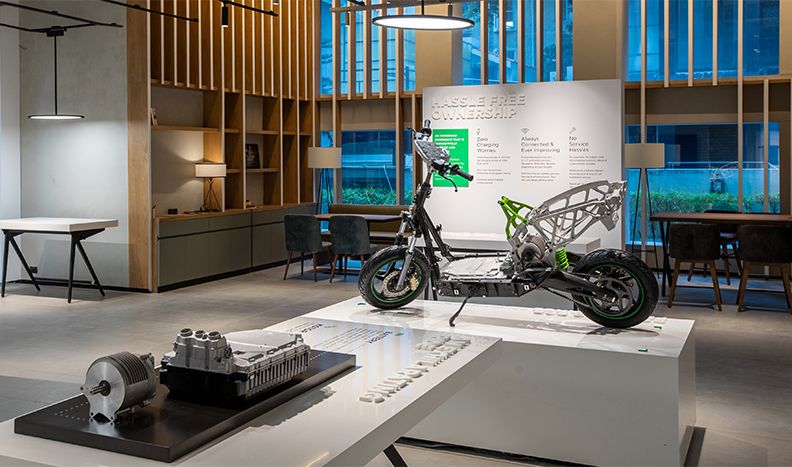 一辆脱光了的踏板车在展览中心的一个平台上展出。前景中的表格显示了电机装配。