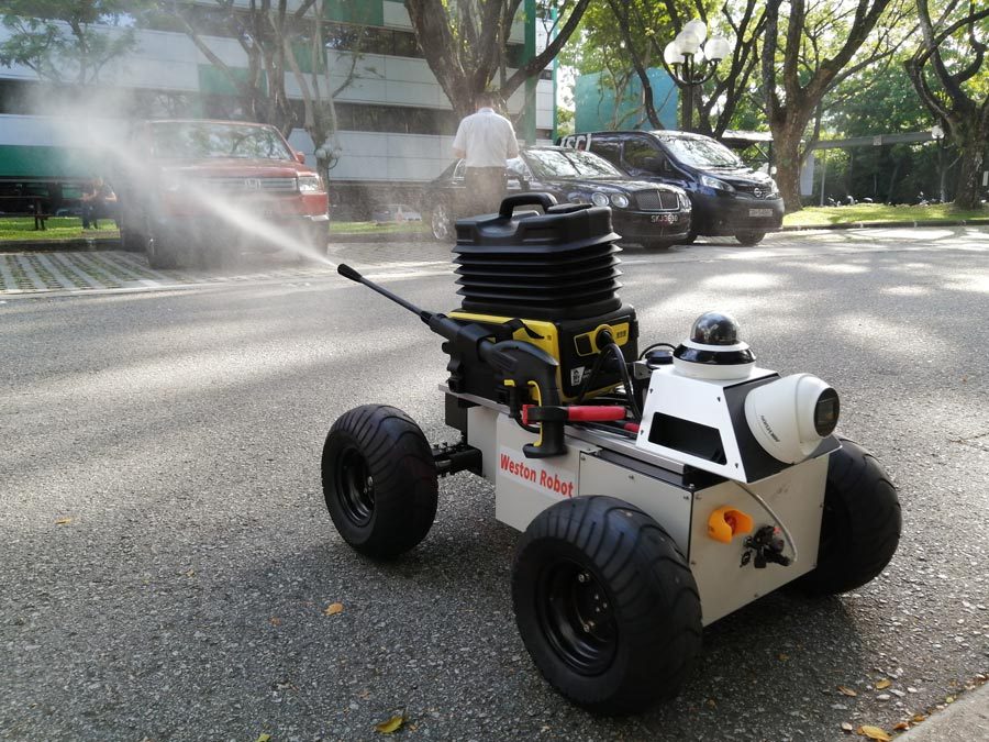 Weston Robot型在铺砌的街道上，积极喷涂外面。汽车和一个人在图像的背景中。